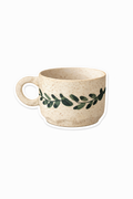 Beige ceramic mug with green leaf design on a white background